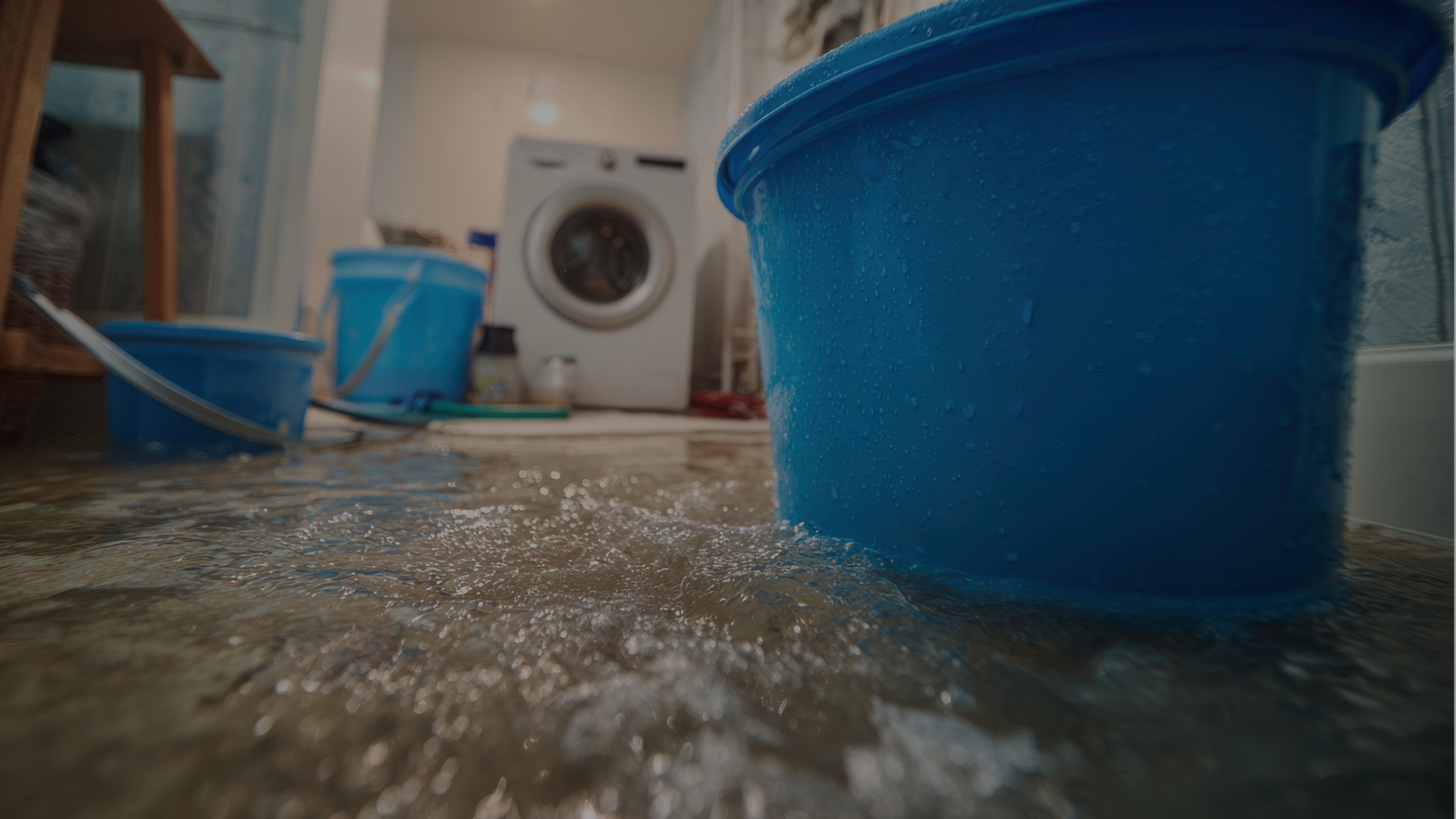 Three blue buckets and a washer in a room that has flooding from a leak. A lot of water damage in a multi family building.