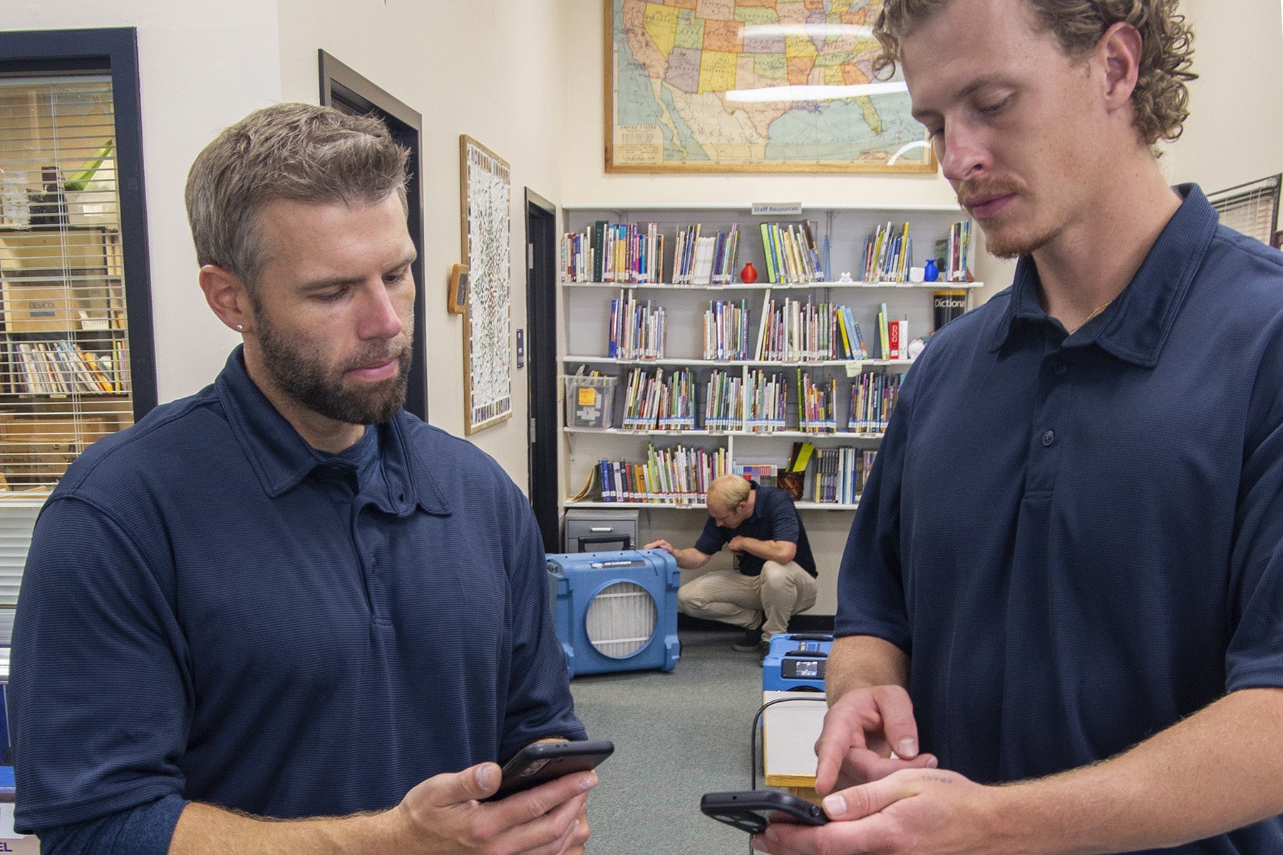 Two people in blue polos checking a moisture meter to see if the damage is dry.