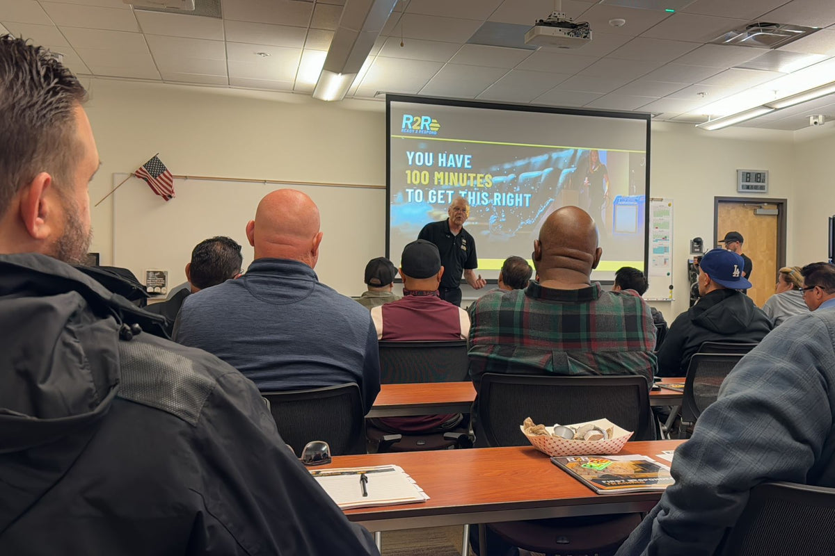 A room full of people watching a presentation. The screen has an R2R (Ready to Respond) logo on top left of the screen. The presentation says "You have 100 minutes to get this right)